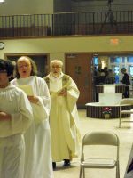 People in white robes walking through a gymnasium with chairs and a balcony in the background