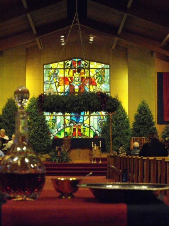 Church sanctuary with Christmas decorations, stained-glass window, and candles on the altar