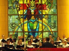 Choir performing in front of a colorful stained-glass mural in an indoor venue