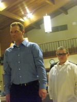 Two people standing indoors under bright ceiling lights, one in a blue shirt and one in a white shirt.