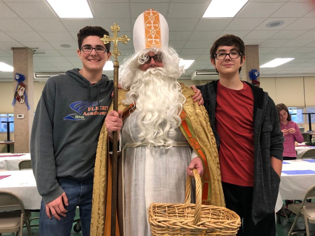 Three people posing indoors, centered on a person in bishop-style costume holding a staff and basket.