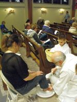 People seated in church pews with one person kneeling to wash another’s feet during a religious service