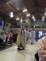 Priest in white and gold vestments walking down church aisle during a procession