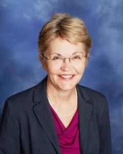 Smiling person in glasses and dark blazer against a blue studio backdrop
