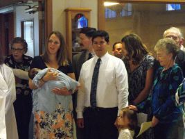 Group of people at an indoor gathering; woman holds a baby, others stand nearby watching.