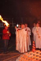 People in robes stand outdoors by a lit torch and orange cones at night