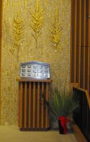 Decorative wall display with golden wheat stalks above a silver donation box and potted plant on a wooden stand
