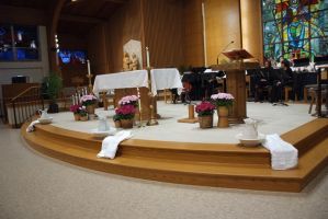Church altar with white cloth, candles, flowers, and stained-glass windows in the background