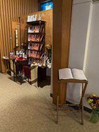 Brochure rack and display stand in a hallway with wood paneling and a small table of flowers