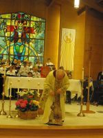 Priest bowing at church altar with stained-glass window and candles in the background