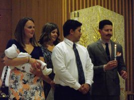 People standing at a formal event, one holding a baby, one man holding a candle.