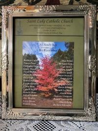 Framed church poster with a tree photo and text titled “Saint Luke Catholic Church” on a lace-covered table