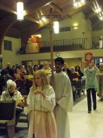Children walking in a church aisle during a procession, with pews and seated adults in the background.