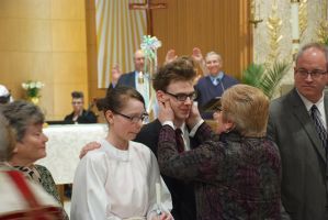 People greeting at a formal indoor ceremony, with one person in a white robe and others in suits and dresses.