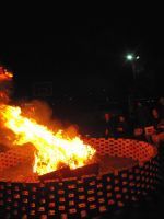 Large fire burning in a metal fire pit at night, with a bright streetlight in the background.