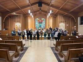 Choir performing in a wooden church sanctuary with stained glass and pews in the foreground