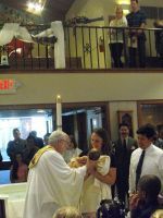 Priest blessing a woman and child in a church ceremony, with onlookers gathered around.