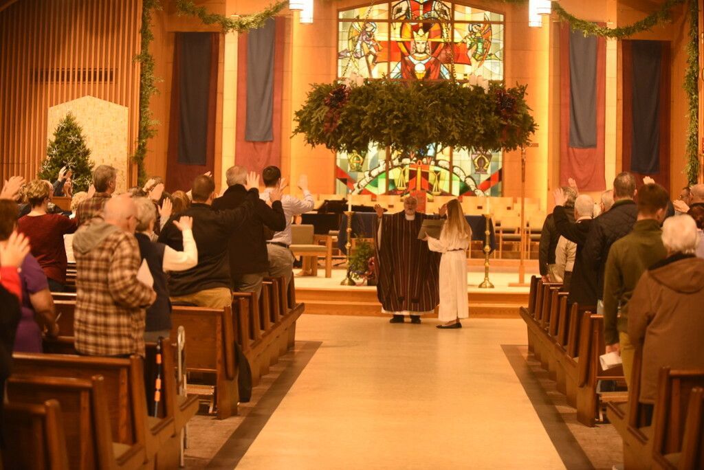 Congregation seated in a decorated church aisle during a wedding ceremony, with an altar and floral arch.