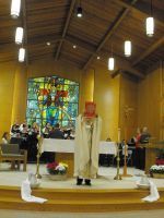 Clergy standing at an altar in a church sanctuary with stained glass and lit candles