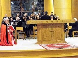 Catholic church ceremony with priest in red vestments at altar, choir seated behind him