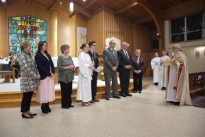 Group of people standing in a church as a priest greets them during a ceremony