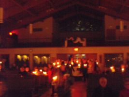 Dimly lit indoor gathering with many people and warm orange lights in a hall or church-like venue