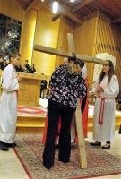 Three people in white robes and a black floral shirt stand in a church aisle during a ceremony