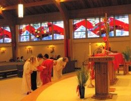 People bow at an altar in a church with red decorations and stained-glass windows.