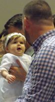 Adult holding a baby in white, facing each other in a crowded indoor setting