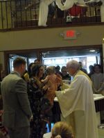 Clergy member in white robe greeting guests at a church entrance during a ceremony