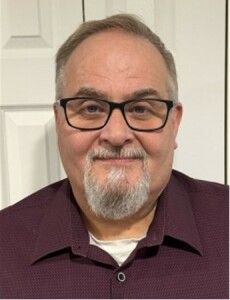 Smiling man with glasses in a burgundy shirt against a light indoor background