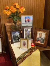 Memorial display with framed photos, flowers, and candles on a small table