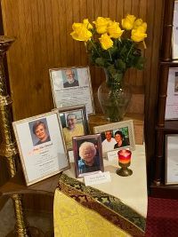 Memorial display with framed photos, yellow roses, and a lit candle on a small table