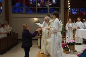 Church communion service with a woman receiving bread from a priest, altar and candles behind them.