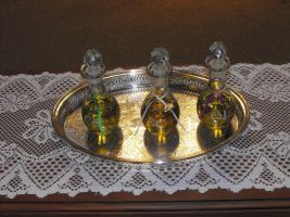 Three decorative glass bottles on a silver tray atop a white lace tablecloth.