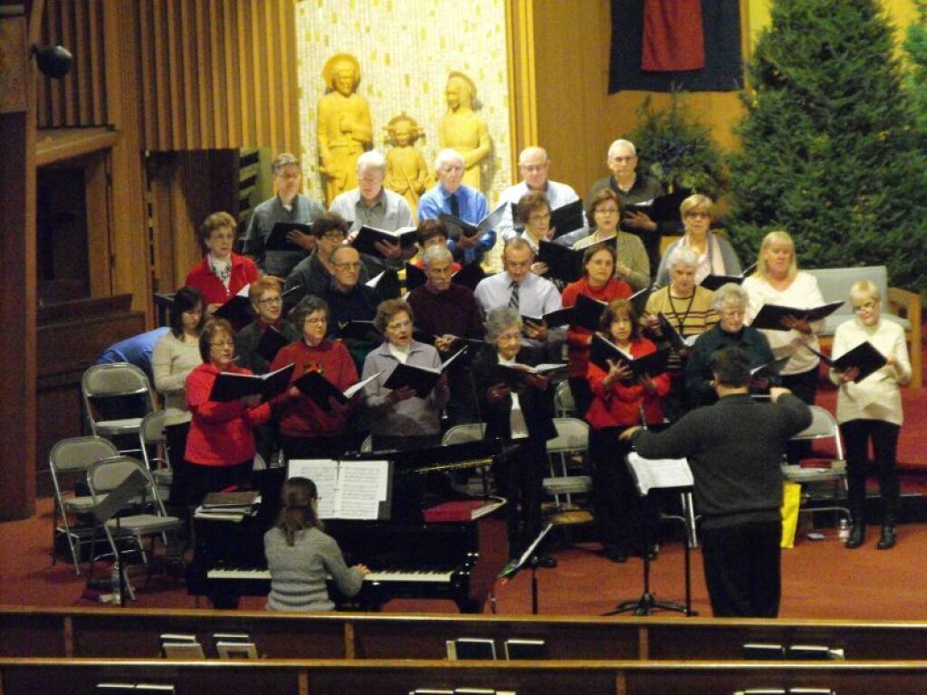 Choir singing on a church stage, with a conductor in front and a Buddha statue in the background.