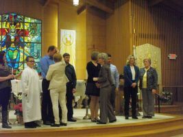 People standing on a church stage during a ceremony, with stained glass in the background.