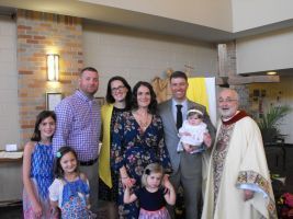 Group posing indoors at a church, including a robed priest holding a baby.