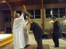 Priest blessing a person with a raised cross in a church, with two others standing nearby