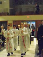 Three martial arts students in white uniforms with red belts walk indoors in a gymnasium.