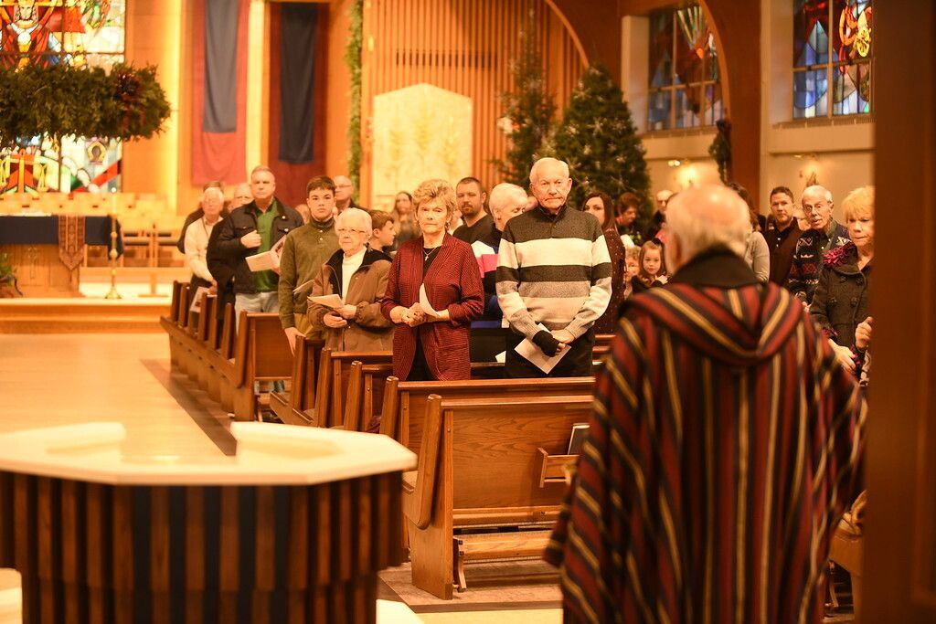 Congregation seated in wooden pews inside a church, facing the altar and a speaker in the foreground.