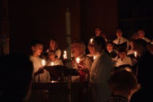 Choir singing by candlelight in a dim church, with music stands and warm glowing candles