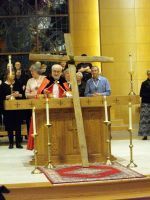 Clergy speak at a church lectern in front of a tall yellow banner and cross-shaped candles.