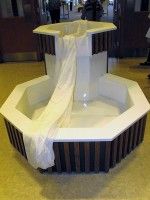 White fountain with flowing water and draped fabric in a hexagonal indoor display.
