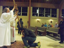 Indoor ceremony with a robed person lifting a tall wooden staff as a kneeling photographer takes a photo