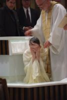Woman kneeling in a white church font while another in white robe pours water on her head during a baptism ceremony