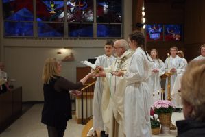Choir members in white robes receive candles from a woman during a church ceremony