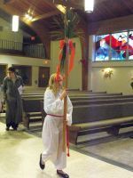 Person in white robe carrying a tall palm leaf in a church aisle during a procession