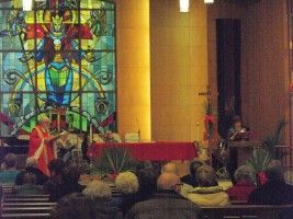 Church service with stained-glass window, altar, and people seated in pews.