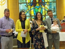 Five people standing in a church, holding papers and a baby during a ceremony
